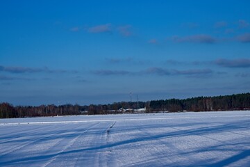 Zimowy, słoneczny dzień. Równina pokryta polami uprawnymi i łąkami pokryta jest warstwą śniegu. - 760094340