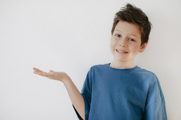 A preschool boy in a blue T-shirt on a light background shows a thumbs up