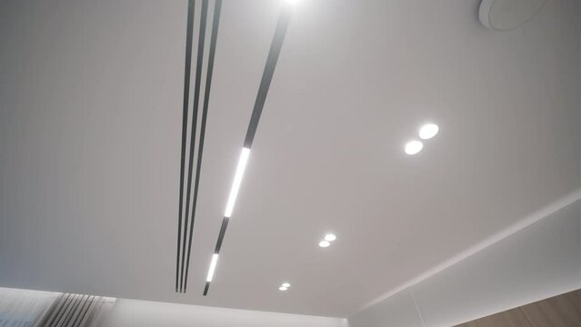 The image shows a close-up view of a modern hallway ceiling with sleek, built-in LED strip lighting and minimalist, dark-colored doors
