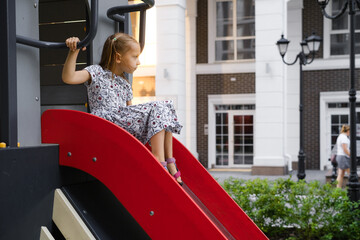 Girl on the slide. Child playing on playground in the city. Preschooler having fun outdoors in summer