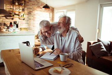 Senior couple laughing and using laptop at home