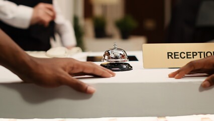 Close up of african american guests ringing concierge bell at reception counter during check in...