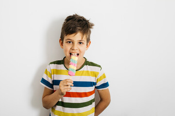 Boy eating ice cream 
Summer treat. A boy in the studio licks colourful ice cream