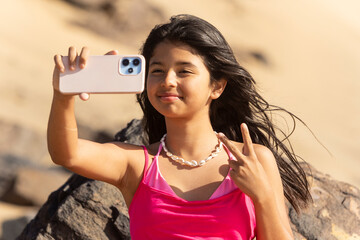 A young girl enjoys the beach vibes as she strikes a playful pose for a selfie, with the sun gently highlighting her features