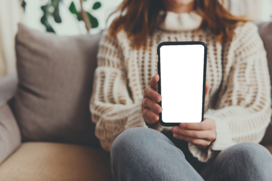 Mockup of a woman's hand holding a smartphone with a transparent screen while sitting on a sofa