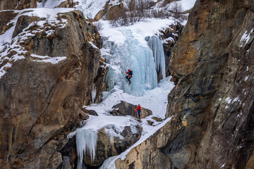 Adventurous climbers ascend a frozen waterfall, their vibrant gear standing out against the icy blue and rocky backdrop