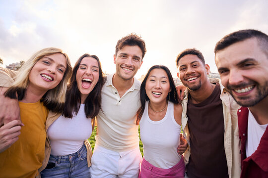 Bunch of happy multiracial friends having fun outdoors at the park. Diverse group of cheerful joyful young people standing up looking at the camera and smiling all together. They are hug and laugh