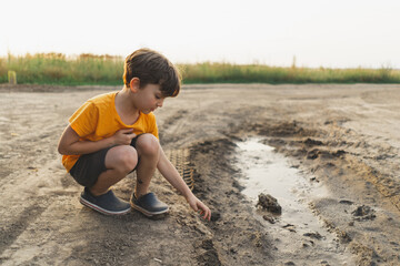 Portrait of a boy in nature. A boy in an orange T-shirt plays with mud in the ground in nature....