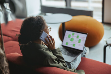 Woman on the couch with a laptop, talking on phone in nice modern coworking office