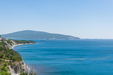 Landscape of the blue sea with a green high coast against the blue sky on a sunny day