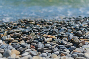 Wet round pebble stones in the foreground are covered by a wave of the blue sea