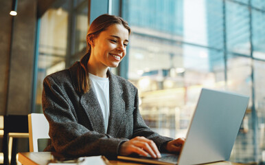 Stylish young female freelancer working on laptop while sitting in cozy cafe 