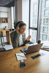 Woman with headphones sits at wood desk using laptop in in nice modern coworking office