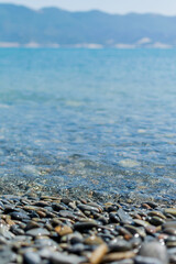 Wet round pebble stones in the foreground are covered by a wave of the blue sea