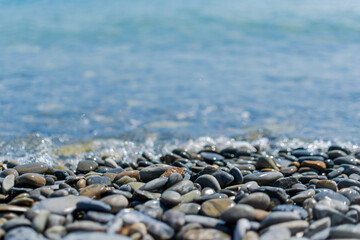 Wet round pebble stones in the foreground are covered by a wave of the blue sea