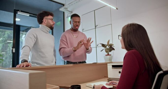 Female, front desk receptionist warmly greeting two diverse, male clients, initiating a friendly conversation in a modern office setting.