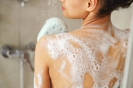 A woman is washing her back with a sponge in the shower