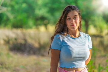 A woman is standing in a field wearing a blue shirt and pink pants