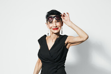 Fashionable mature woman in black dress and sunglasses posing with hands on head for camera...