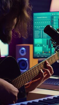 Vertical Video Artist composing a song with his acoustic guitar in home studio, recording notes and singing melody on microphone. Sound engineer mixing and mastering his tunes with stereo equipment
