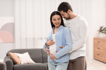 Happy pregnant woman with her husband at home, space for text