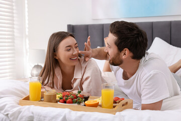 Obraz na płótnie Canvas Happy couple eating tasty breakfast on bed at home