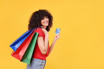 Happy young woman with shopping bags and credit card on yellow background. Space for text