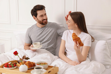 Obraz na płótnie Canvas Happy couple having tasty breakfast in bed at home