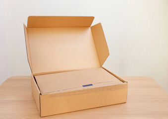 Open cardboard box with item wrapped in kraft paper on wooden table, space for text. Delivery service