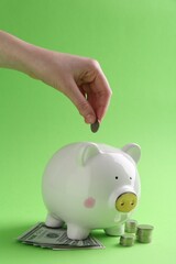 Financial savings. Woman putting coin into piggy bank on green background, closeup