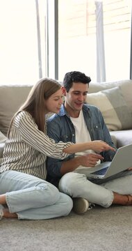 In living room young Hispanic couple sits comfortably engaged in modern e-commerce through their laptop, consider products and services, booking tickets for weekend trip, select goods for their home