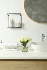 Bouquet of beautiful roses in vase and bath accessories near sink in bathroom