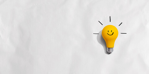 Yellow light bulb with happy face - flat lay - obrazy, fototapety, plakaty