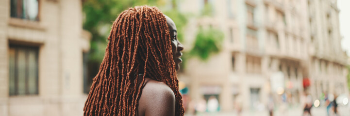 Woman with African braids wearing top crosses the road at crosswalk, Panorama