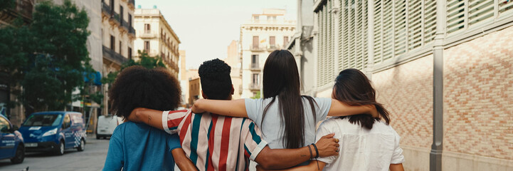 Happy multiethnic young people walk embracing on summer day outdoors, Back view, Panorama. Group of...