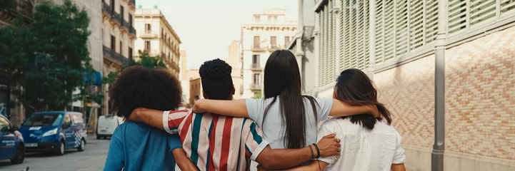 Foto op Canvas Happy multiethnic young people walk embracing on summer day outdoors, Back view, Panorama. Group of friends are talking and laughing merrily while walking along on the street © Andrii Nekrasov
