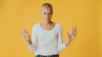 Young hairless woman listens carefully and strongly disagrees, looking at camera isolated on yellow...
