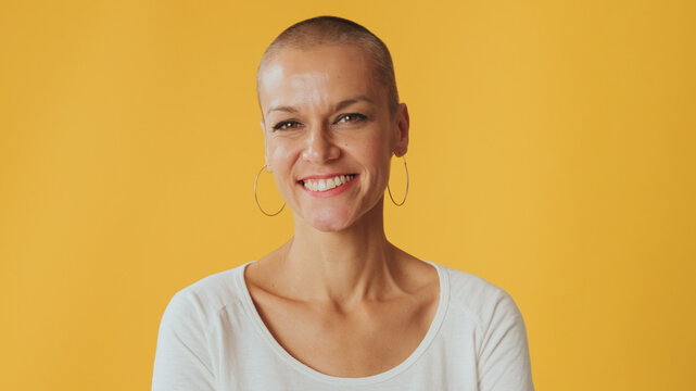 Close up, young hairless woman looks at camera isolated on yellow background in studio