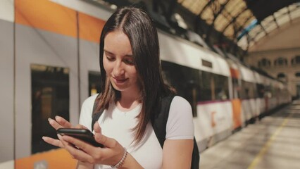 Close up, young woman scrolling mobile phone while standing on the platform of the railway station