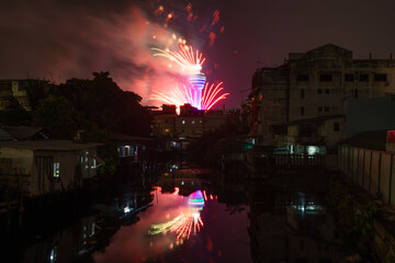 Fireworks celebration at Samut Prakan Observation Tower with river reflection in urban city town, Thailand.