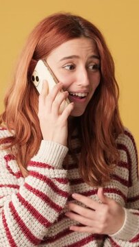 Happy girl receiving good news by mobile phone on yellow background