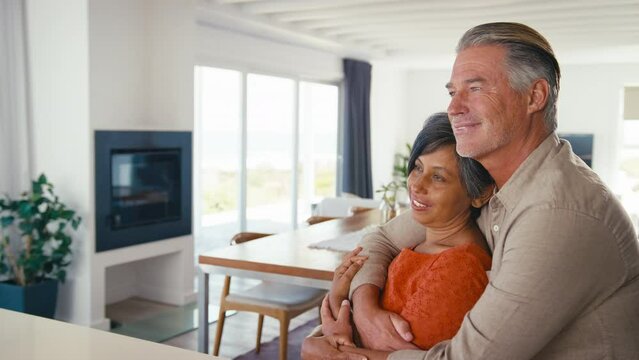 Happy and loving mature couple sitting by counter at home hugging - shot in slow motion