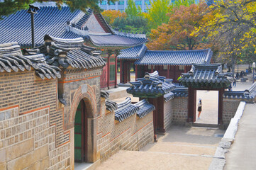 Old ancient palace gate and building of Deoksugung palace with colourful trees foliage in Autumn. There is a tourist stands in the picture.