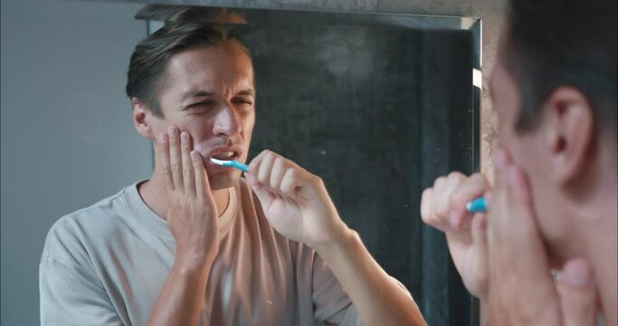 Guy carefully brushes his teeth in bathroom, but has problem. Man problem with painful due to hypersensitive gums. This common problem makes guys uncomfortable during their daily oral hygiene routine.