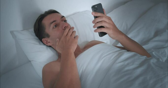 Man has been lying in bed since morning and, opening mobile phone, reads shocking news. Shocking headlines make us think about future. Shocking facts on screen make reconsider your plans for day.