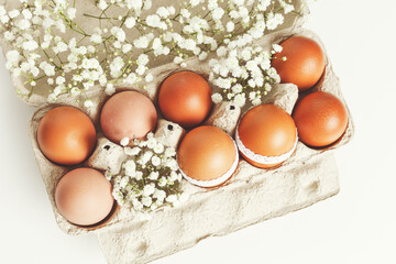 Brown Easter eggs decorated lace and white gypsophila flowers in carton on white background. Easter...