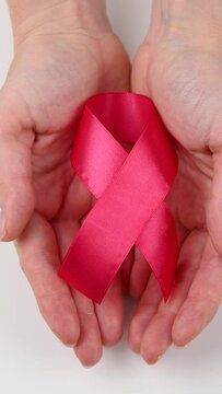 Close-up of female hands with pink ribbon on a white background. Symbol of the fight against breast cancer. Vertical video. 
