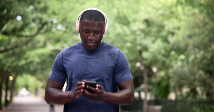 Headphones, black man and cellphone on run for music, fitness and wellness outdoor for workout. Male person, runner and athlete strong for exercise, health or training for cardio with mobile