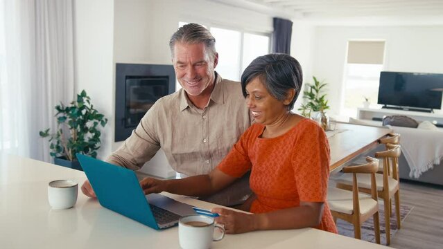 Excited mature couple with laptop at home using credit card to book vacation tickets or shop online - shot in slow motion