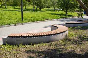 Close-up of a brown wooden bench in the shape of an arc in a summer city park